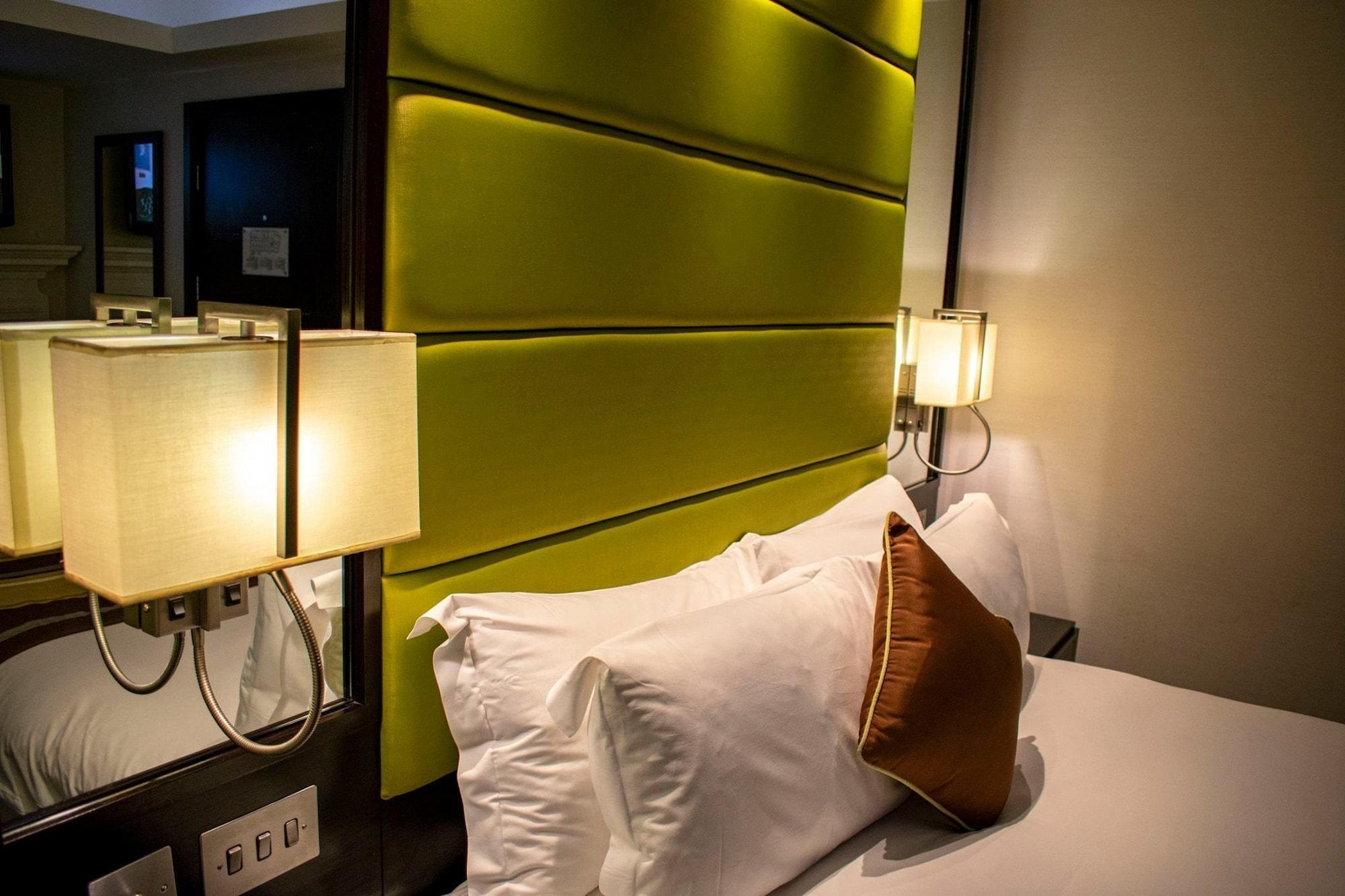 ホテル Montcalm Brewery Townhouse ロンドン エクステリア 写真 The photo shows a modern hotel room with a stylish design. The focal point is a large bed with white pillows and a decorative brown pillow. The headboard is bright green and has a textured appearance. On either side of the bed, there are wall lamps t