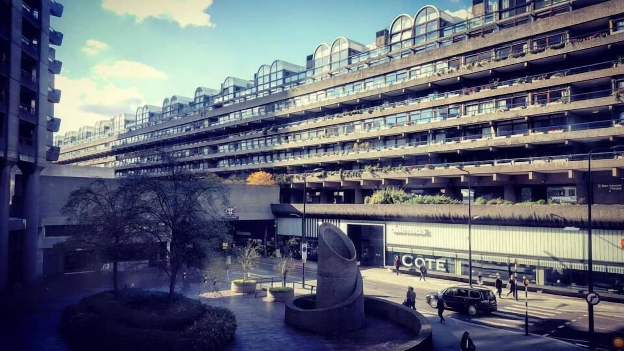 ホテル Montcalm Brewery Townhouse ロンドン エクステリア 写真 The photo shows a modern architectural structure with multiple levels, featuring a series of large, rectangular balconies. Below this building, there is a plaza or courtyard area with a sculptural piece, which appears to be made of stone. Surrounding