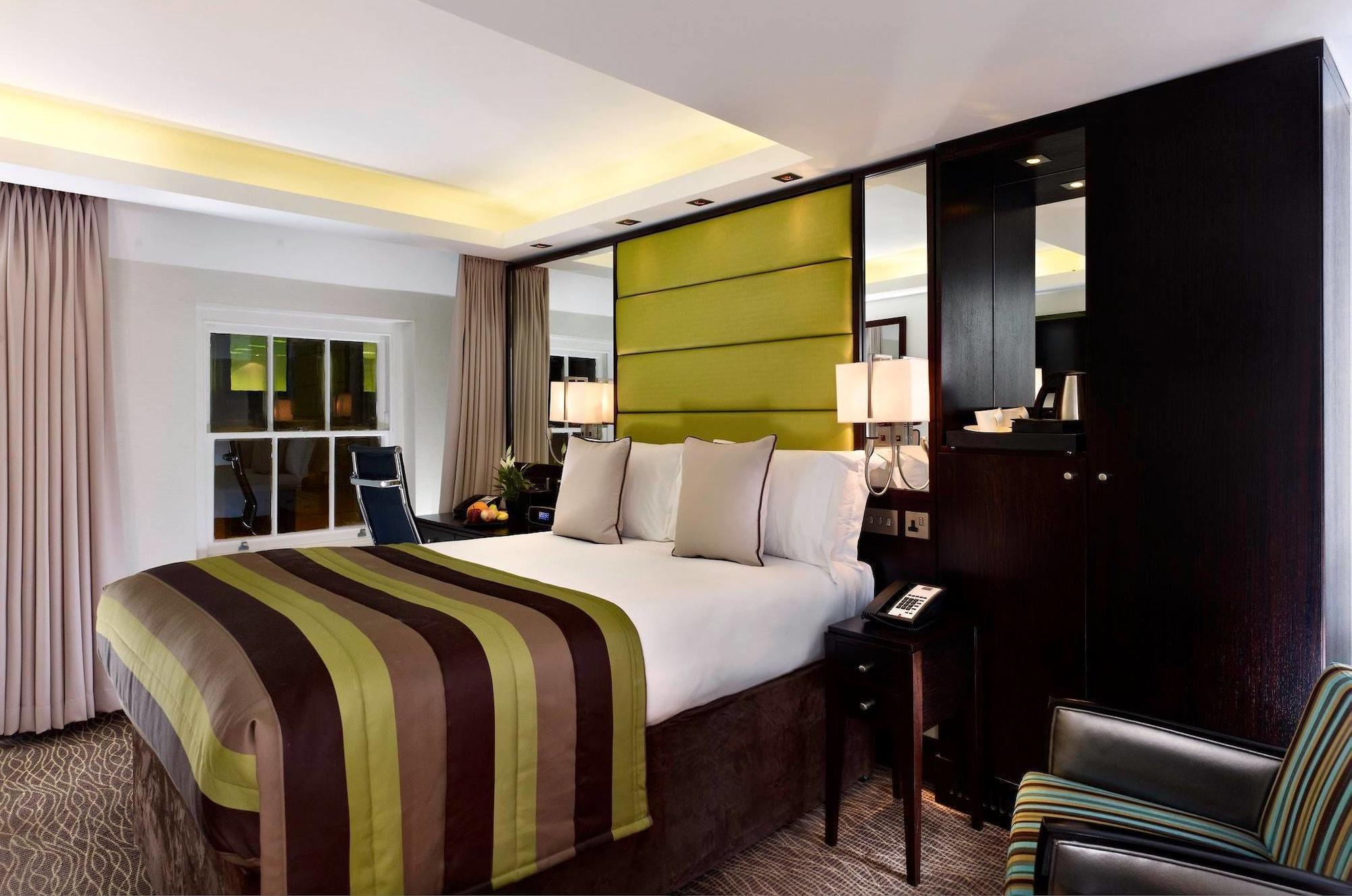 ホテル Montcalm Brewery Townhouse ロンドン エクステリア 写真 The photo shows a modern hotel room featuring a large bed with a striped comforter in shades of green, brown, and cream. The bed is adorned with several decorative pillows. Behind the bed, there is a contemporary headboard with a green panel design. 