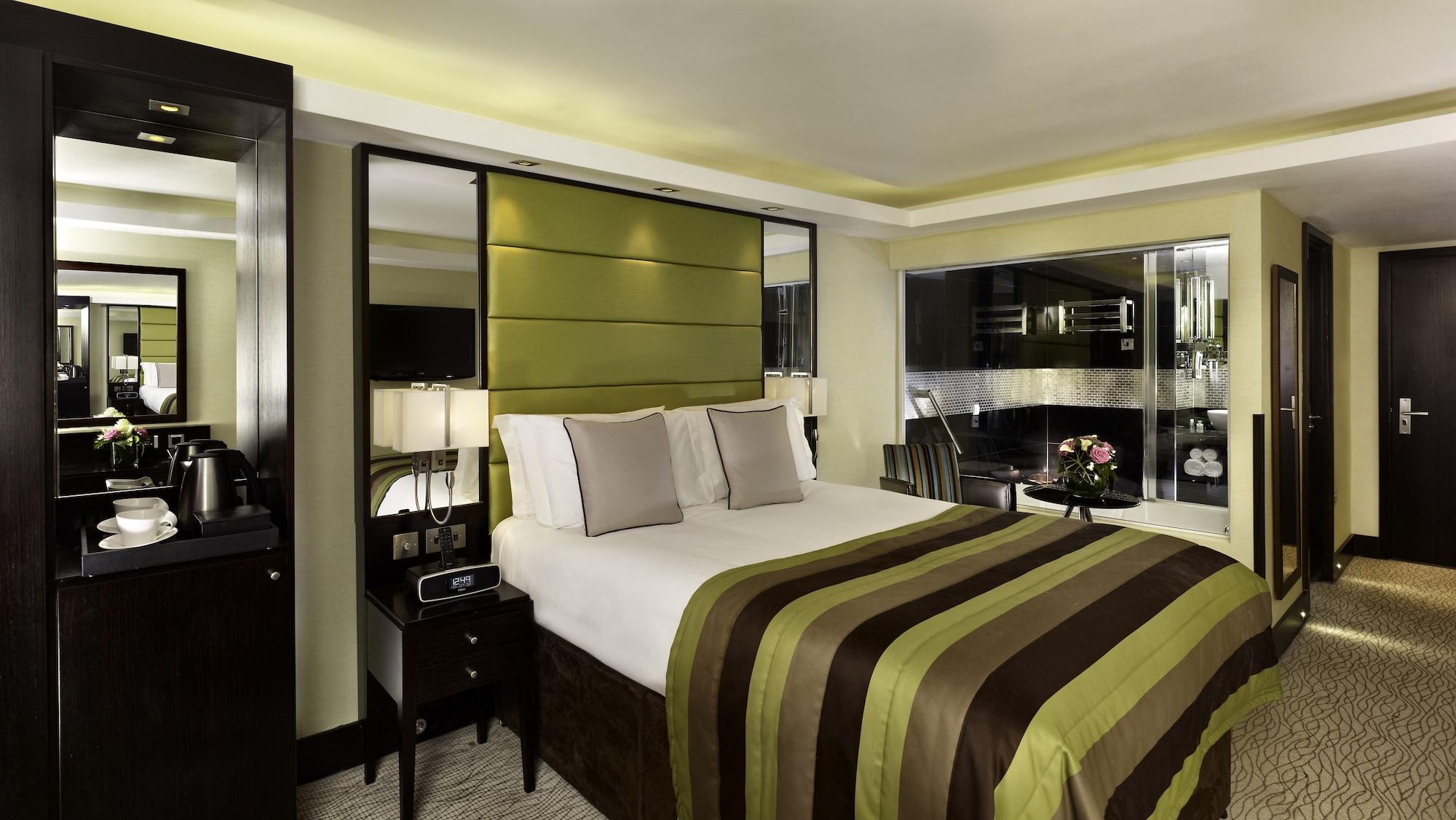 ホテル Montcalm Brewery Townhouse ロンドン エクステリア 写真 The photo shows a modern hotel room designed with a sophisticated aesthetic. It features a comfortable double bed with a striped brown and green bedspread, complemented by two light gray decorative pillows. Behind the bed is an elegant headboard sect