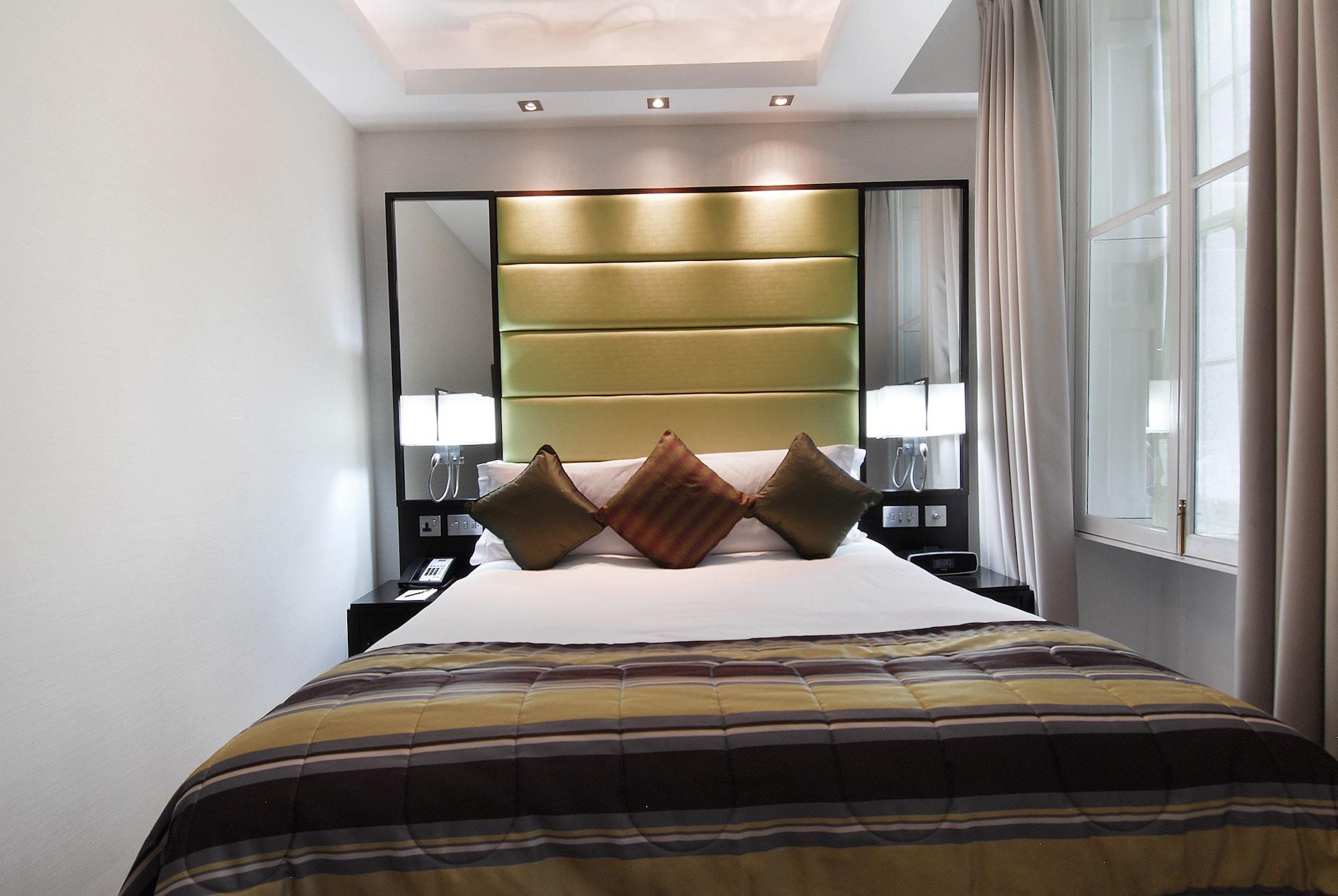 ホテル Montcalm Brewery Townhouse ロンドン エクステリア 写真 The photo shows a stylishly decorated bedroom. The bed is centered in the room, featuring a white comforter with a plaid pattern in shades of brown and green. There are three decorative pillows on the bed, two in shades of brown and one in dark green