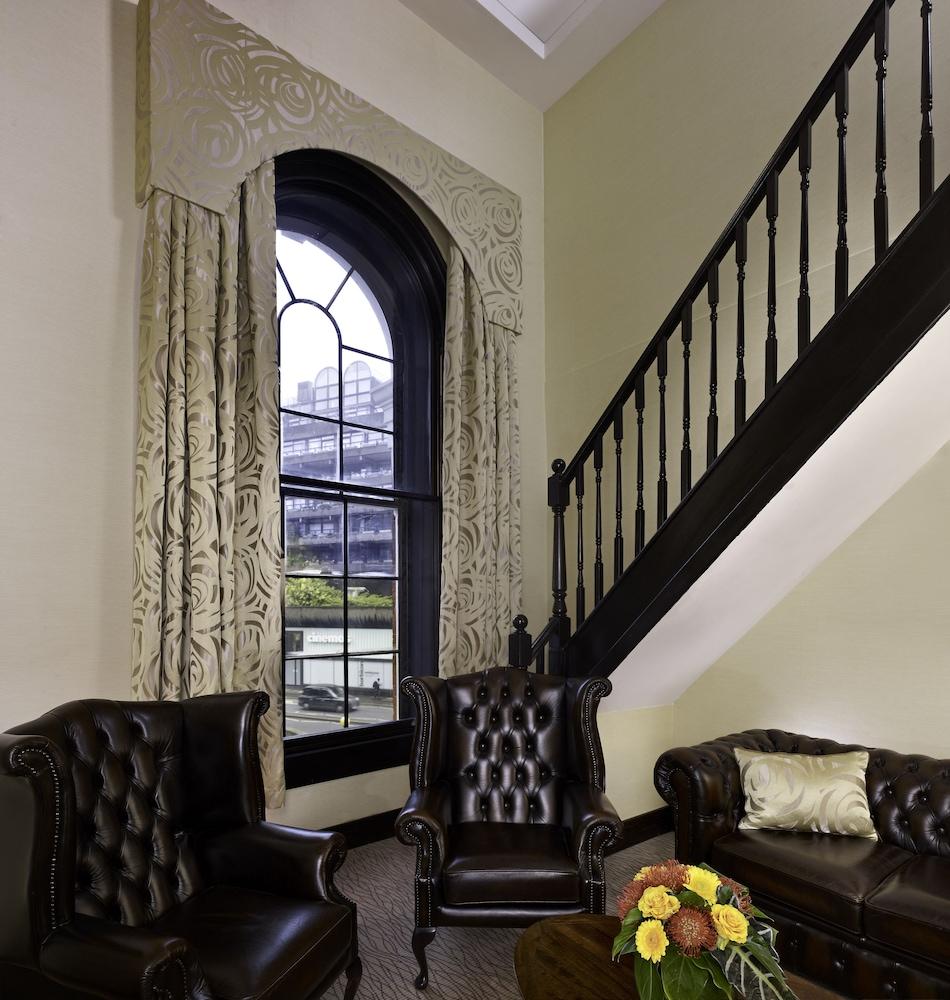 ホテル Montcalm Brewery Townhouse ロンドン エクステリア 写真 The photo shows a cozy interior space featuring two elegant leather armchairs placed near a large, ornate window with arched top and decorative curtains. The wall is painted in a muted color, enhancing the warmth of the room. A staircase with black s