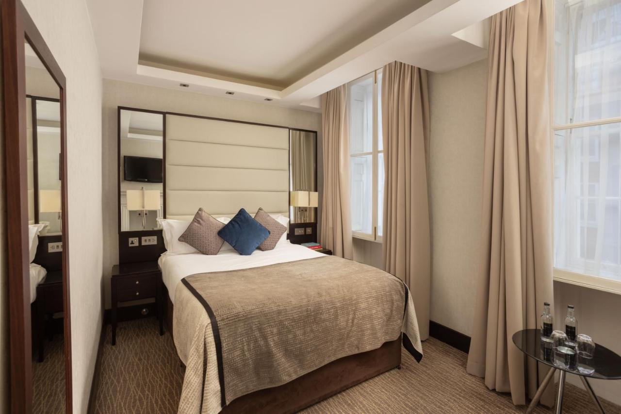 ホテル Montcalm Brewery Townhouse ロンドン エクステリア 写真 The photo shows a cozy hotel bedroom. The room features a neatly made double bed with a beige bedspread and decorative pillows, including a blue one. There are bedside tables on either side of the bed with lamps. The walls are painted in a soft color