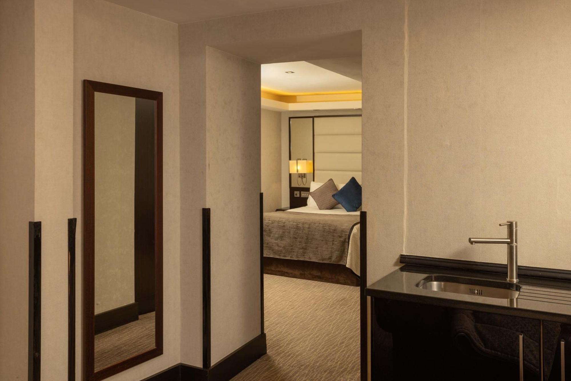 ホテル Montcalm Brewery Townhouse ロンドン エクステリア 写真 The photo shows an interior space that appears to be part of a hotel room or suite. There is a doorway leading into a bedroom area, where a bed with decorative pillows is visible. In the foreground, there's a tall mirror on the left side and a small 