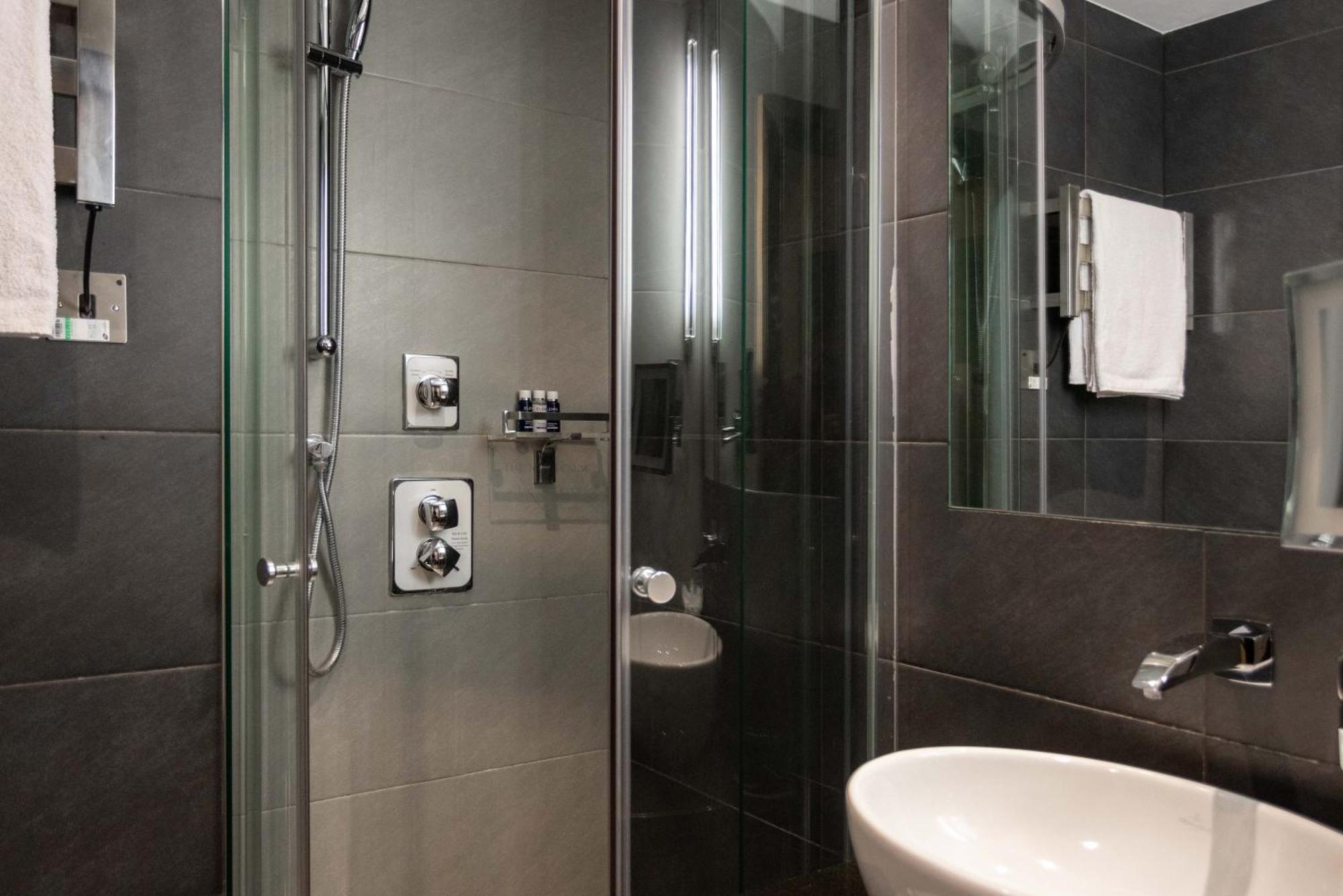 ホテル Montcalm Brewery Townhouse ロンドン エクステリア 写真 The photo shows a modern bathroom with a glass shower enclosure. The shower features a handheld showerhead and various controls mounted on the wall. The walls are tiled in dark, sleek tones, contributing to a contemporary aesthetic. There is a round 