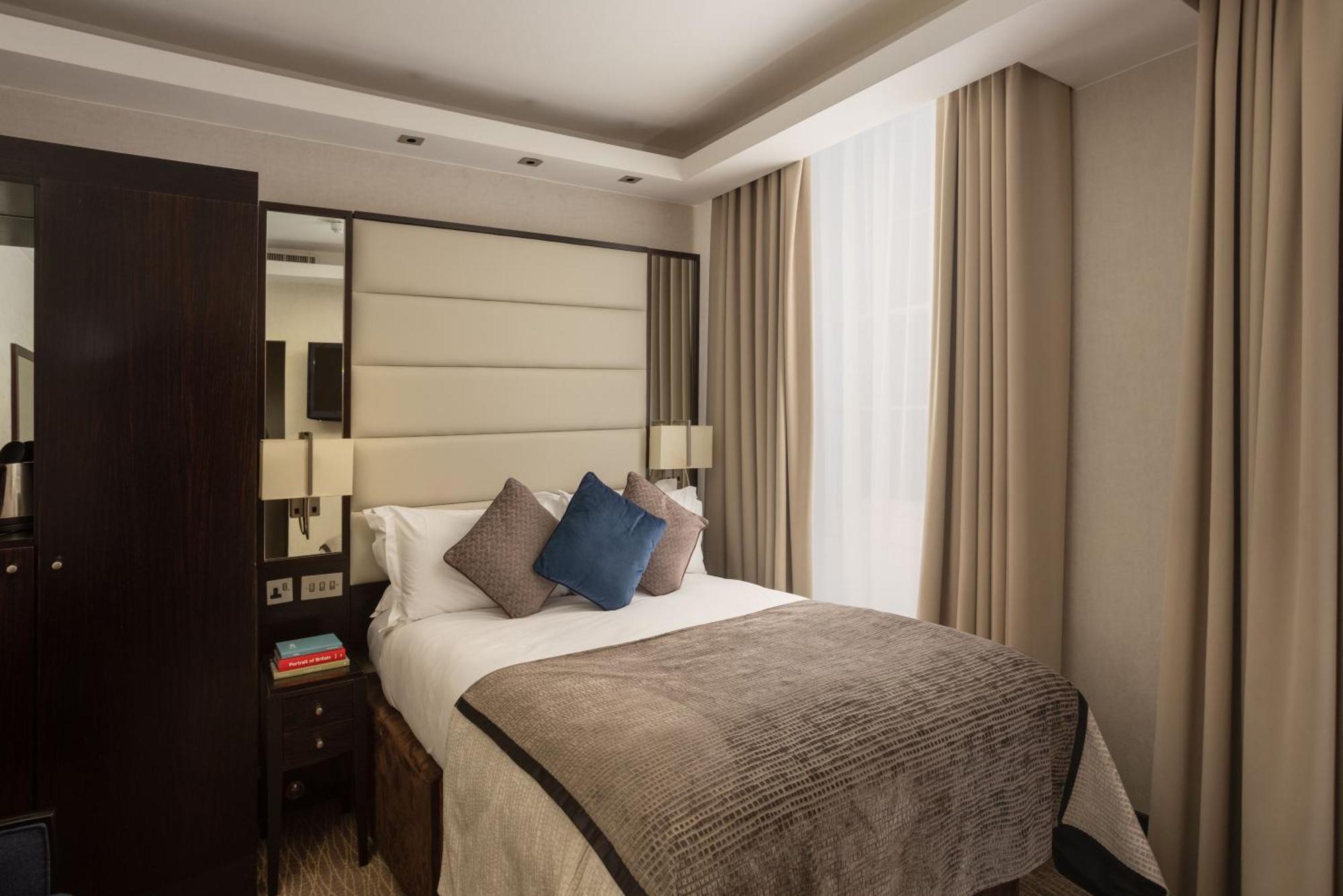 ホテル Montcalm Brewery Townhouse ロンドン エクステリア 写真 The photo shows a modern hotel room with a cozy design. It features a double bed with a light-colored headboard and a soft, stylish blanket. There are decorative pillows on the bed, including a blue one. On either side of the bed, there are small nig