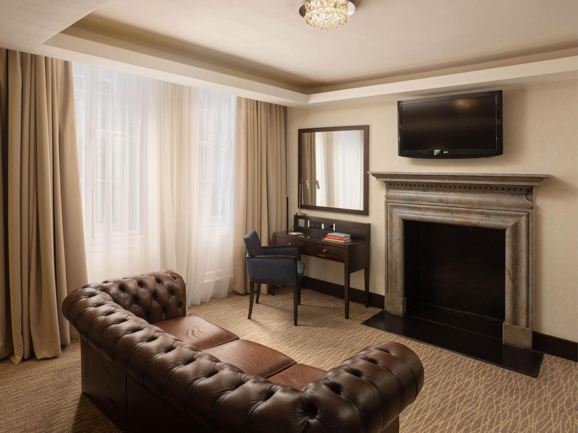 ホテル Montcalm Brewery Townhouse ロンドン エクステリア 写真 The photo shows a cozy and elegantly designed room. There is a comfortable brown leather sofa with tufted detailing. A small desk and chair are positioned near a mirror, providing a space for work or personal grooming. On the wall, a flat-screen TV i