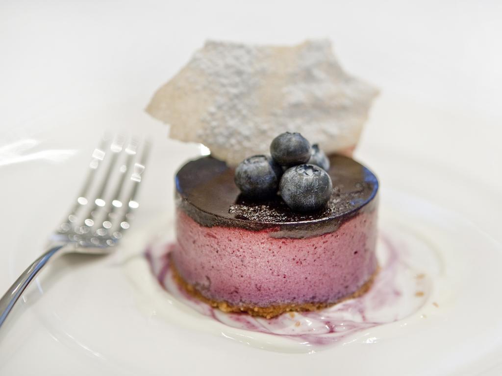 ホテル Montcalm Brewery Townhouse ロンドン エクステリア 写真 The photo shows a beautifully plated dessert, which appears to be a round cheesecake or mousse. It has a pinkish-purple filling, topped with a glossy dark chocolate layer. Three fresh blueberries sit on top, adding a pop of color. The dessert is acco