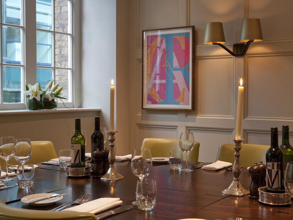 ホテル Montcalm Brewery Townhouse ロンドン エクステリア 写真 The photo shows an elegantly set dining room with a large wooden table surrounded by several chairs. The table is adorned with neatly arranged utensils, glasses, and decorative items. There are two tall candlesticks with candles and several bottles o
