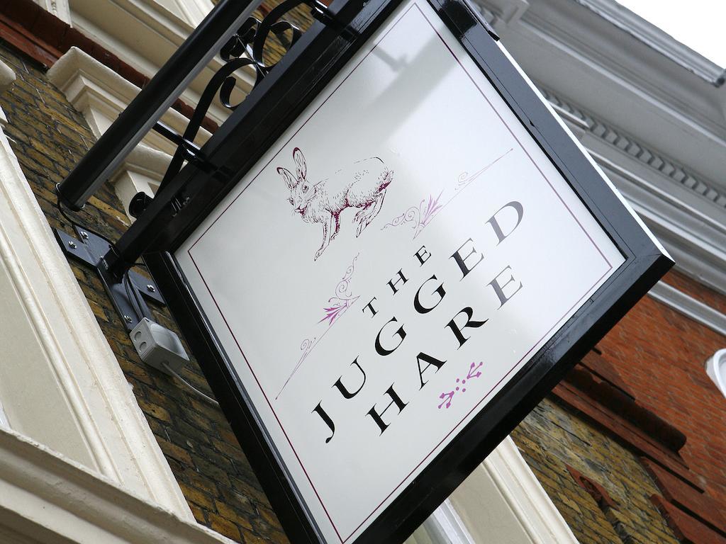 ホテル Montcalm Brewery Townhouse ロンドン エクステリア 写真 The photo shows a hanging sign for a place called "The Jugged Hare." The design features an illustration of a hare, along with the name displayed prominently in bold letters. The overall aesthetic combines an elegant font with delicate floral accents