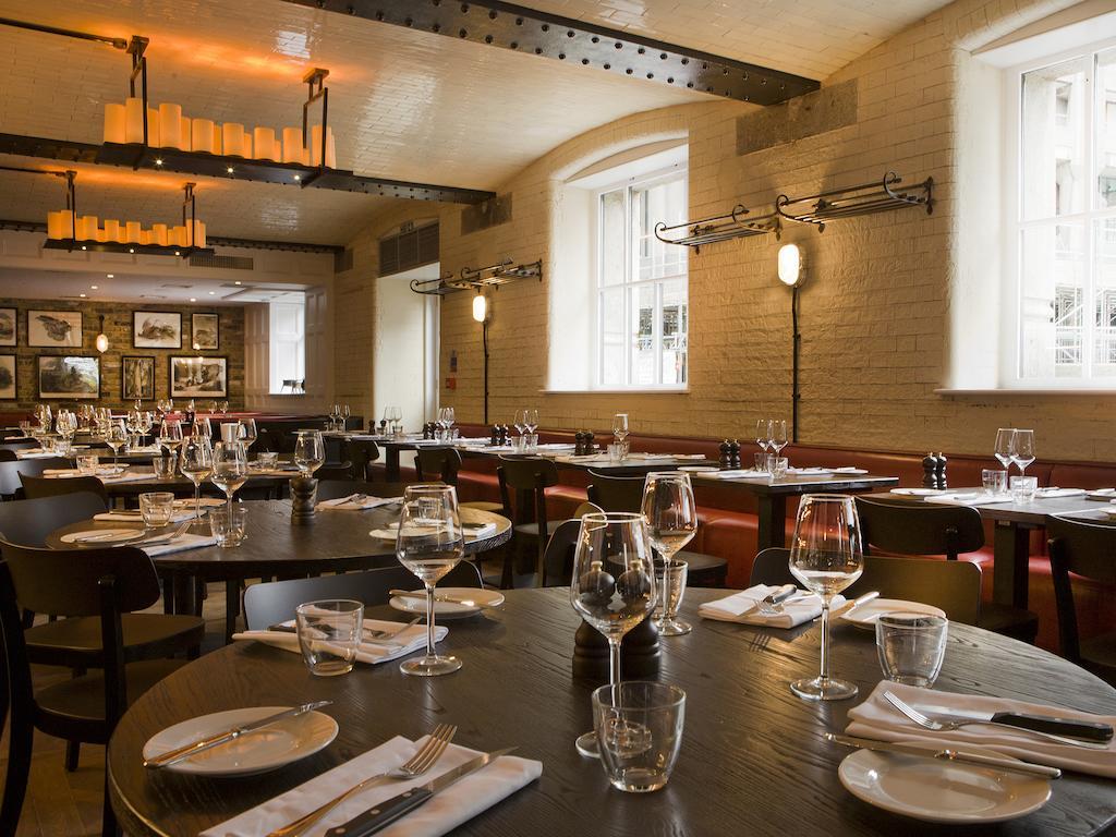 ホテル Montcalm Brewery Townhouse ロンドン エクステリア 写真 The photo shows a restaurant interior featuring a warm and inviting atmosphere. It has several round wooden tables set for dining, each with neatly arranged plates, utensils, and glasses. The lighting is soft, with overhead fixtures providing a cozy 