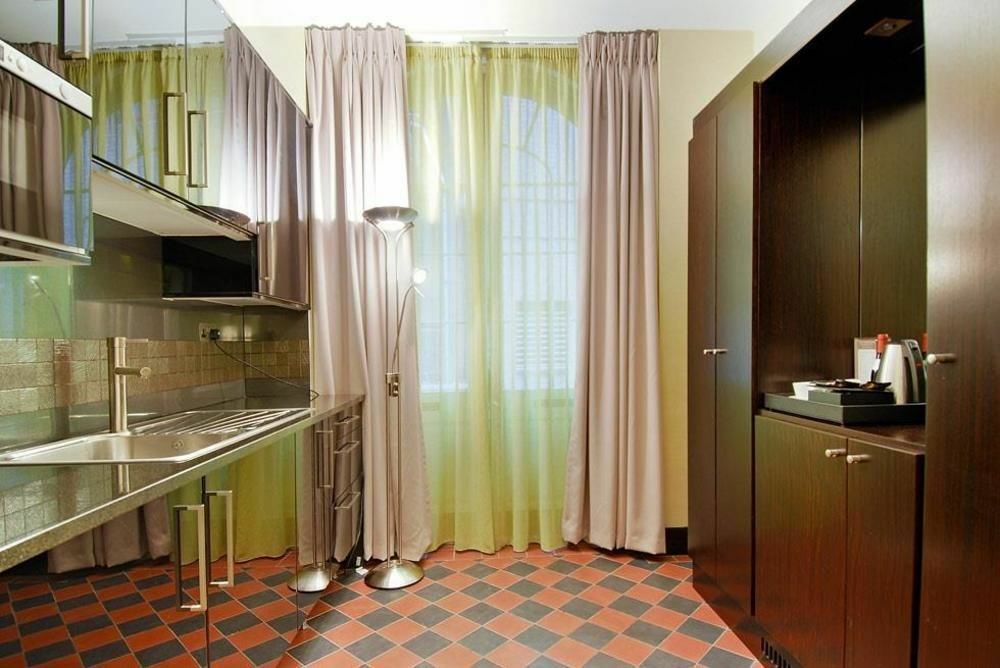 ホテル Montcalm Brewery Townhouse ロンドン エクステリア 写真 The photo shows a modern kitchen area. There is metallic cabinetry and a stainless steel countertop with a sink. The walls are adorned with light-colored curtains that allow natural light to filter in, with one set in a soft purple hue and another in
