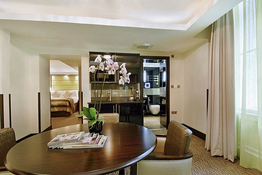 ホテル Montcalm Brewery Townhouse ロンドン エクステリア 写真 The photo shows a stylish hotel room or suite. In the foreground, there is a round dining table with a few magazines on it. Surrounding the table are upholstered chairs. To the right, there are large windows with light-colored curtains, allowing natu