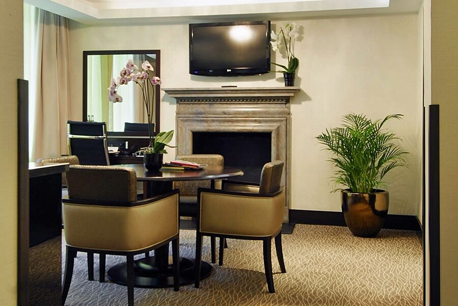 ホテル Montcalm Brewery Townhouse ロンドン エクステリア 写真 The photo shows a modern and stylish room with a dining or meeting area. There is a round table surrounded by four upholstered chairs. A flat-screen television is mounted on the wall above a decorative fireplace. To the side, there is a mirror reflec